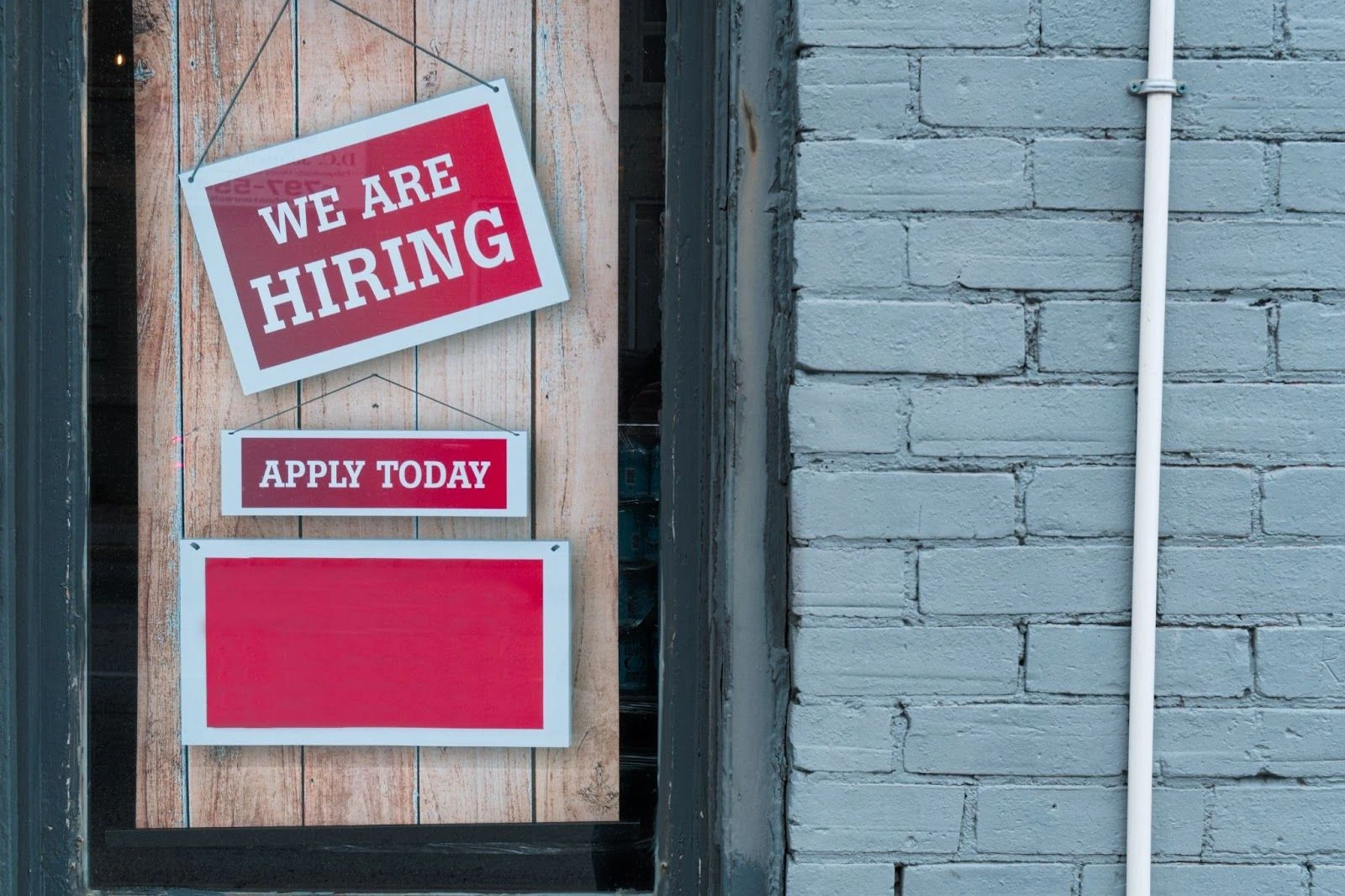 A “We Are Hiring” red sign hung on a window. Despite the effects of the Great Resignation, hiring statistics for startups remain positive. Image from Unsplash